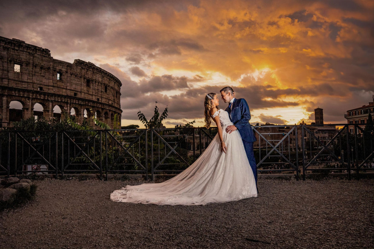 Fotografía nocturna de pareja frente al Coliseo iluminado con velo en movimiento.