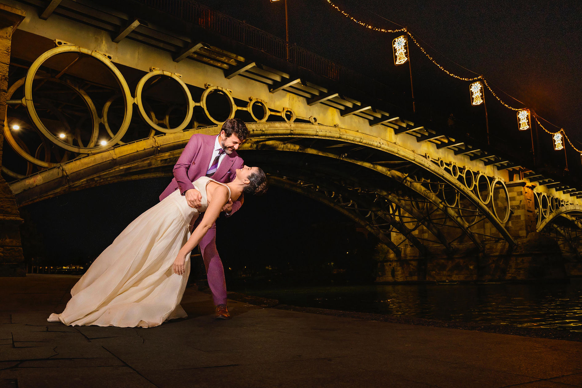 Pareja caminando bajo el Puente de Triana con luces nocturnas.