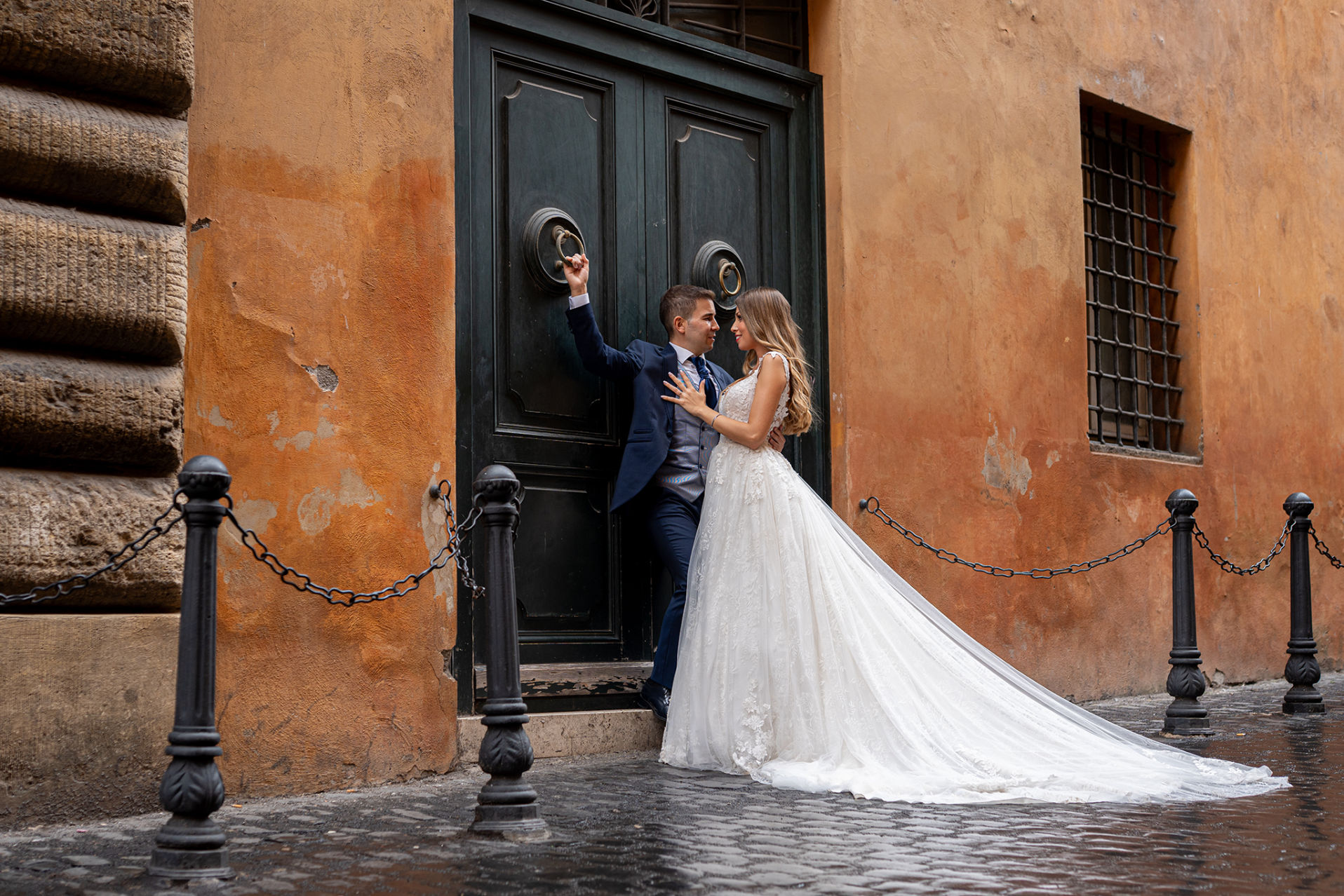 Pareja de novios posando en Via Giustiniani, Roma, junto a una puerta antigua de tono anaranjado.